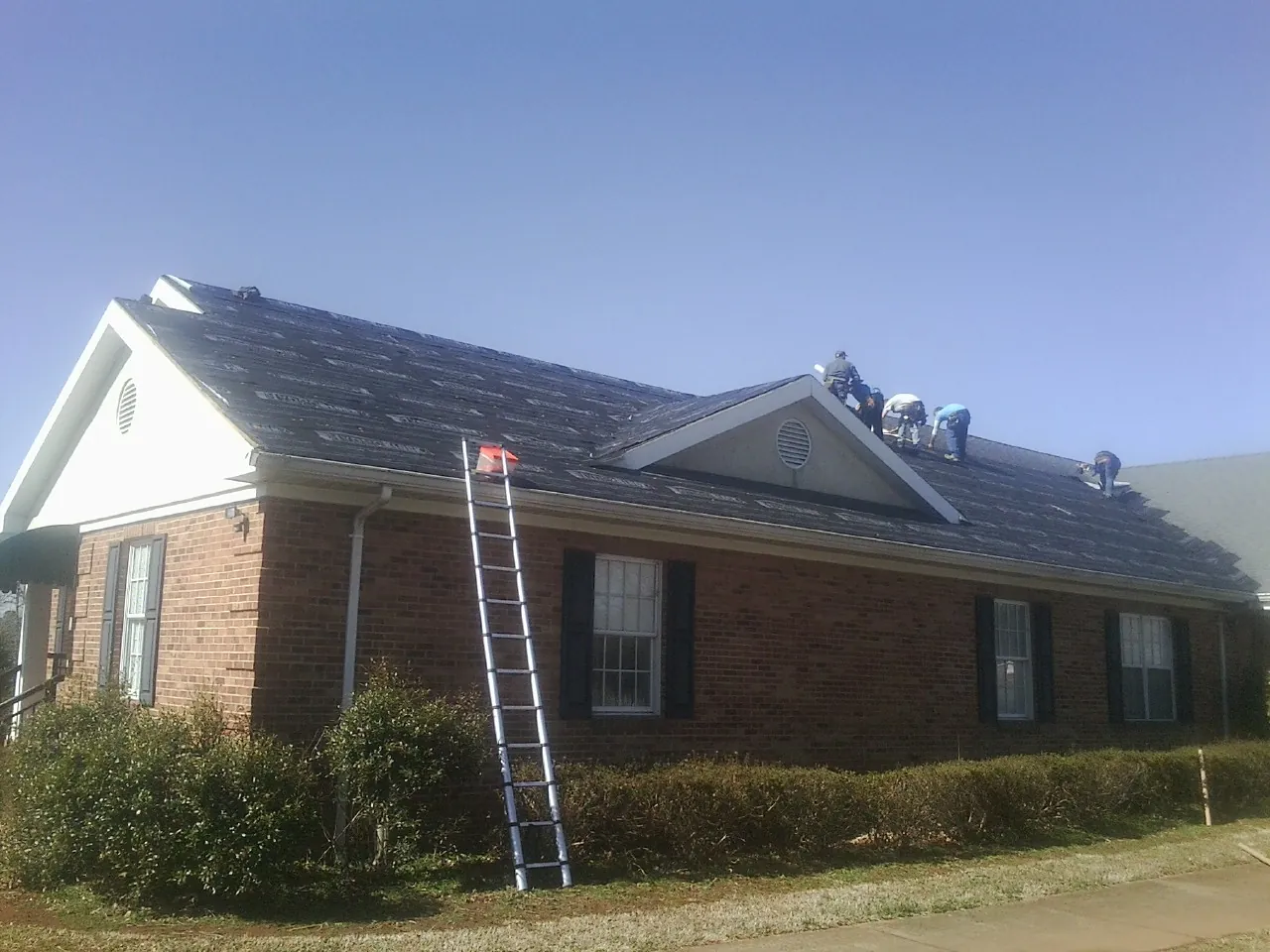 Crew tearing shingles off a brick ranch roof with a ladder set — Metal Roof Repair work by our crew in Sabinsville