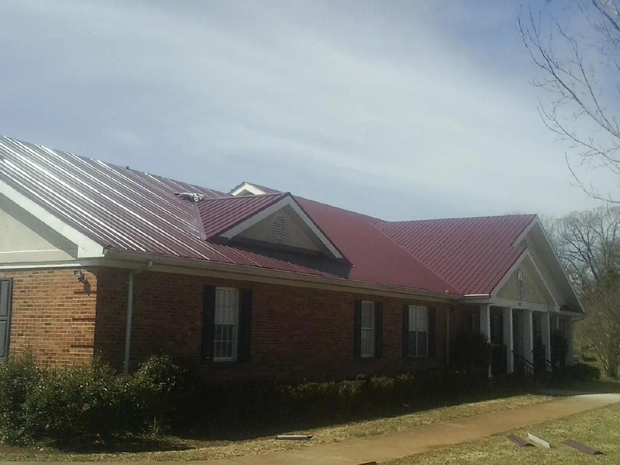Red metal roof with gabled entries on a long brick building, from a Hail Damage Roof Repair job in Sabinsville