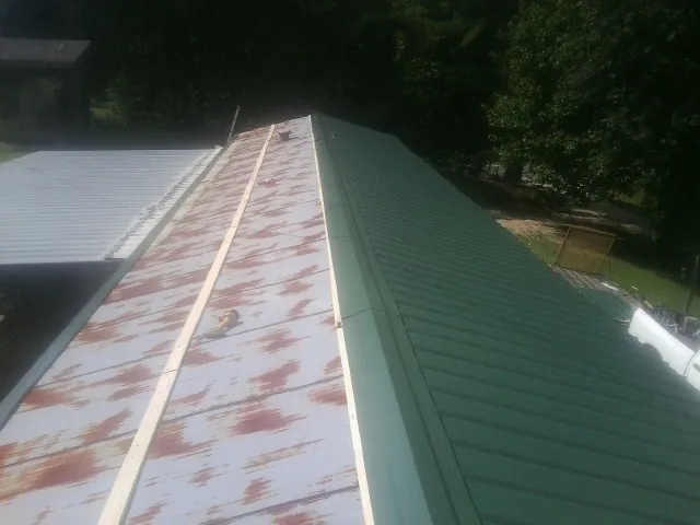 Old rusted panels beside newly installed green metal roofing — Wind Damage Roof Repair by Roofing Brothers in Sabinsville