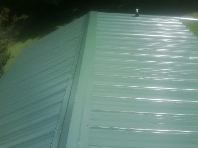 New green metal panels meeting at the ridge of a roof — Flat Roof Repair work by our crew in Sabinsville