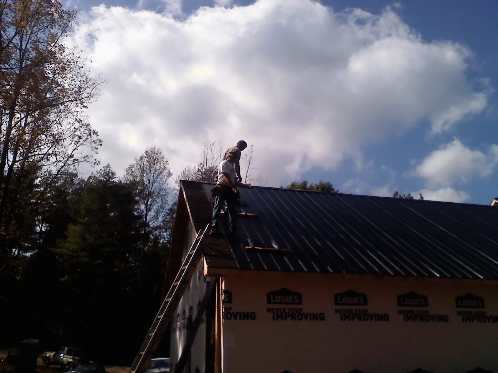 Roofer fastening dark metal panels high against a cloudy sky, from a Roof Inspection job in Sabinsville