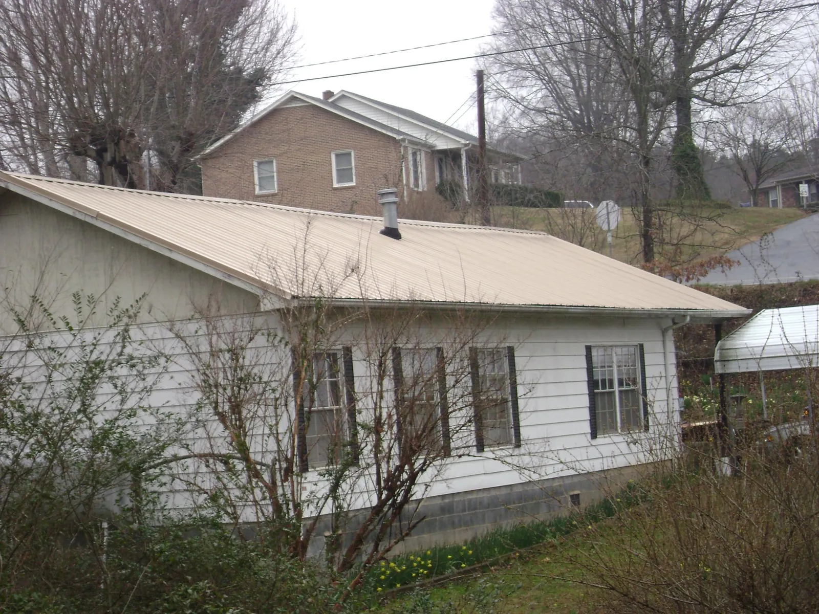 Tan metal roof on a white sided house set into a hillside — Commercial Roofing by Roofing Brothers in Sabinsville